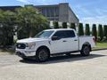 A white 2021 Ford F-150 pickup truck parked with a large cab and bed featuring black wheels and chrome accents