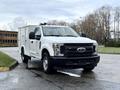 A white 2017 Ford F-350 SD with a service body parked on a wet surface showcasing its rugged design and large front grille