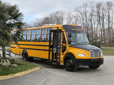A 2022 Freightliner B2 school bus in bright yellow with black accents parked with its door open