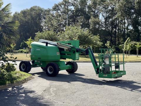 A green 2015 JLG 450AJ cherry picker with an extended platform and large tires positioned on a road