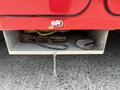 A red storage compartment under a truck contains wooden planks a rope and a metallic hook with a chain hanging down