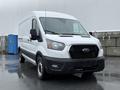 A white 2022 Ford Transit van is parked in the foreground with a front view showcasing its grille headlights and large cargo space