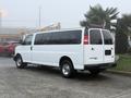A white 2016 GMC Savana van with a long body and large windows parked on a flat surface showcasing its rear and side features