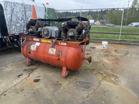 A 2000 Baldor Air compressor with two large motors mounted on top and a rusted metal tank with visible labels and a valve on the side