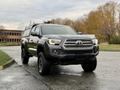 A 2016 Toyota Tacoma truck with a silver grille and a black exterior parked on a wet surface with trees in autumn foliage in the background
