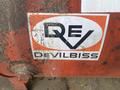 A weathered Devilbiss logo featuring an orange oval with the letters REV prominently displayed in white and black against a textured surface