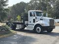A white 2020 Peterbilt 330 flatbed truck with a black metal side rail and orange marker lights