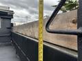 A 2015 Mitsubishi Fuso FE160 truck with a wooden flatbed measuring tape standing against the side of the truck's bed