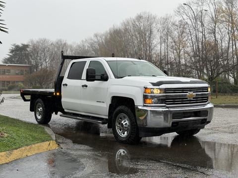 A 2015 Chevrolet Silverado white pickup truck with a flatbed in the foreground standing on a wet surface