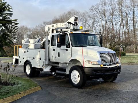 A 2013 International Durastar 4300 utility truck with a white exterior featuring a boom lift apparatus and storage compartments on the side