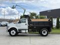 A white 2017 Ford F-750 dump truck with a black bed and wooden sides is parked, showing a side profile view of the vehicle