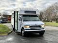 A white 2002 Ford Econoline shuttle bus with an open door and large windows parked on a paved surface