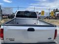 A white 2007 Ford F-350 SD with an open truck bed is parked and facing away from the viewer showing the rear view and taillights