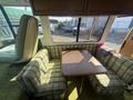 Interior of a 1976 GMC Motorhome featuring a green plaid seating area with a wooden table in the center and large windows providing light