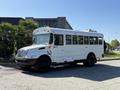 A 2013 International CE300 school bus with a white exterior and black wheels stands parked with several windows on the side and lights on the roof.