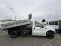 A 2004 Ford F-350 SD dump truck with an elevated bed showing its cargo area and a single cab with a driver visible inside the vehicle
