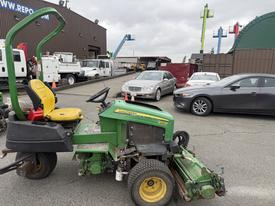 A 2009 John Deere 2653B Precision turf mower with a yellow seat and green body is parked in a lot surrounded by vehicles and equipment