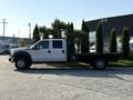 A 2014 Ford F-550 flatbed truck is parked with a dual cab design featuring black flatbed and white cabin with large tires