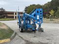 A blue 2016 Genie TZ-34/20 aerial lift with outriggers extended and a platform mounted at the top positioned on a concrete surface