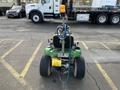 A 2021 John Deere L Series S riding lawn mower with a green body and yellow seat visible from the back with a hose attached and a safety light on top