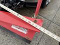 A red snow plow blade attached to a vehicle with a measuring tape resting on it displaying measurements up to 16 inches
