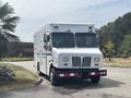A white 2011 Workhorse W62 delivery truck with multiple windows a flat front and a red and white striped bumper parked on a paved surface