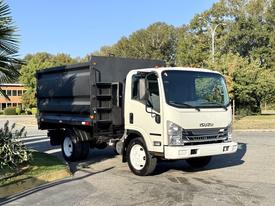 A 2017 Isuzu NPR HD truck with a white cab and a black dump bed is parked at an angle showcasing its front and side features