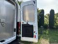 The rear door of a 2016 Ford Transit 150 is open revealing a large cargo space with a silver metallic interior and a black panel on the side