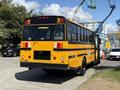 A yellow 2011 Freightliner B2 school bus is parked with its rear facing the viewer showcasing its large windows and emergency exit doors