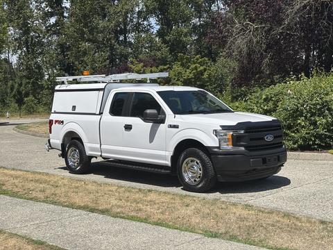 A white 2019 Ford F-150 with a ladder rack on the roof and a utility bed designed for work or service purposes