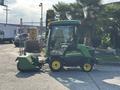 A 2021 John Deere 1575 lawn mower with a cab and front-mounted mower deck in green and yellow colors parked on a paved surface