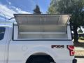 A 2019 Ford F-150 with an open truck bed cover displaying an empty silver storage compartment
