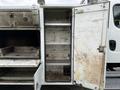 A 2005 Freightliner M2 106 with an open storage compartment revealing empty shelves and a worn interior surface