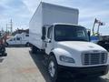 A 2017 Freightliner M2 106 truck with a large white cargo box and a rounded front design parked in a lot with other vehicles in the background