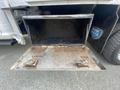 A metal storage compartment with a hinged door and two latches is open on the side of a 2016 RAM 5500 truck with an interior showing worn surfaces and debris