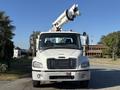 A 2006 Freightliner M2 106 bucket truck with a raised boom and an extended arm facing forward, featuring a white cab and dark tinted windows
