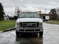 A white 2008 Ford F-350 pickup truck with a flatbed is parked with its front facing the camera and has amber lights on the top of the cab