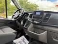 Interior view of a 2021 Ford Transit with a steering wheel dashboard and multimedia display showing controls and gear shift