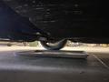 A 1968 Ford Mustang viewed from underneath showing the undercarriage and a tire with an oil catch pan on the ground beneath it