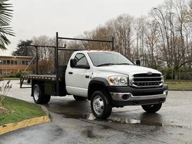 A white 2008 Sterling Bullet flatbed truck with a black flatbed and orange lights on the roof positioned on a paved surface