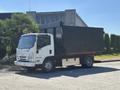 A white 2016 Isuzu NPR-HD truck with a large black dump body is parked on a paved surface