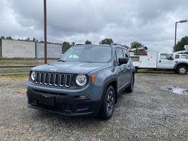 A 2018 Jeep Renegade in a gray color with black accents showcasing its distinctive grille and headlights parked on gravel ground