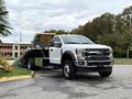 A 2022 Ford F600 tow truck with a flatbed, featuring a white exterior and chrome accents, facing the viewer with its flatbed slightly lowered