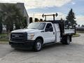 White 2015 Ford F-350 truck with a flatbed and tool boxes on the side parked on a paved area