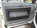 The interior door panel of a 2015 Ford F-450 featuring a black handle storage compartment and textured surfaces in a light gray color