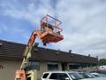 A 2009 JLG E300AJP aerial lift is positioned with its platform elevated at a commercial building