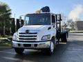 A 2015 Hino 358 flatbed truck with a white exterior and chrome grille parked with its flatbed visible and a hydraulic lift in the back