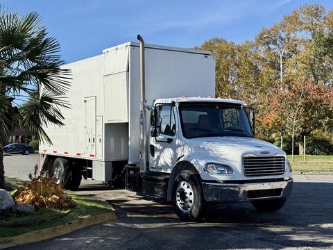 A white 2011 Freightliner M2 106 box truck with a large cargo area and a tall exhaust pipe parked on a street