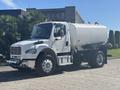 A white 2022 Freightliner M2 106 tank truck with a rounded tank and chrome details is parked at an angle showing its side profile and large tires