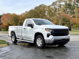 A 2024 Chevrolet Silverado 1500 pickup truck in white with a black grille and chrome accents parked on a wet surface